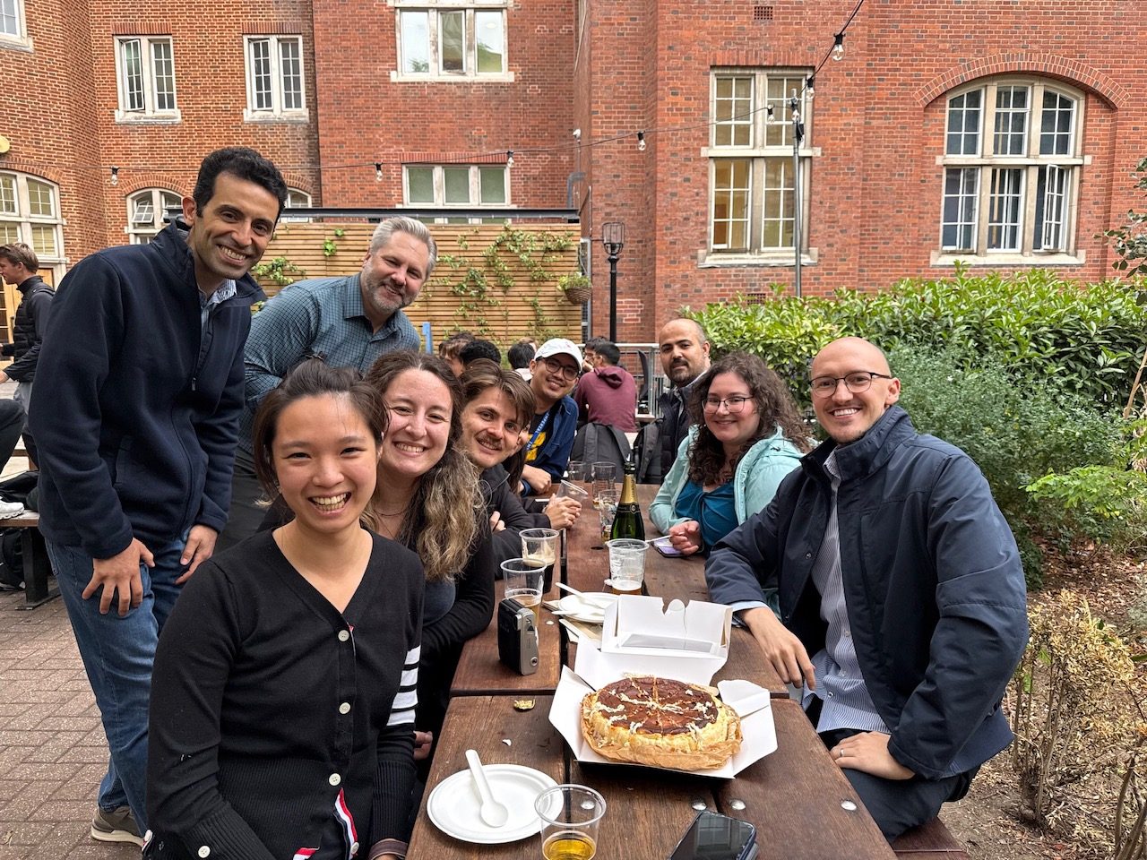 The lab celebrating Emily's viva in a college courtyard, with a celebratory pie on the table.