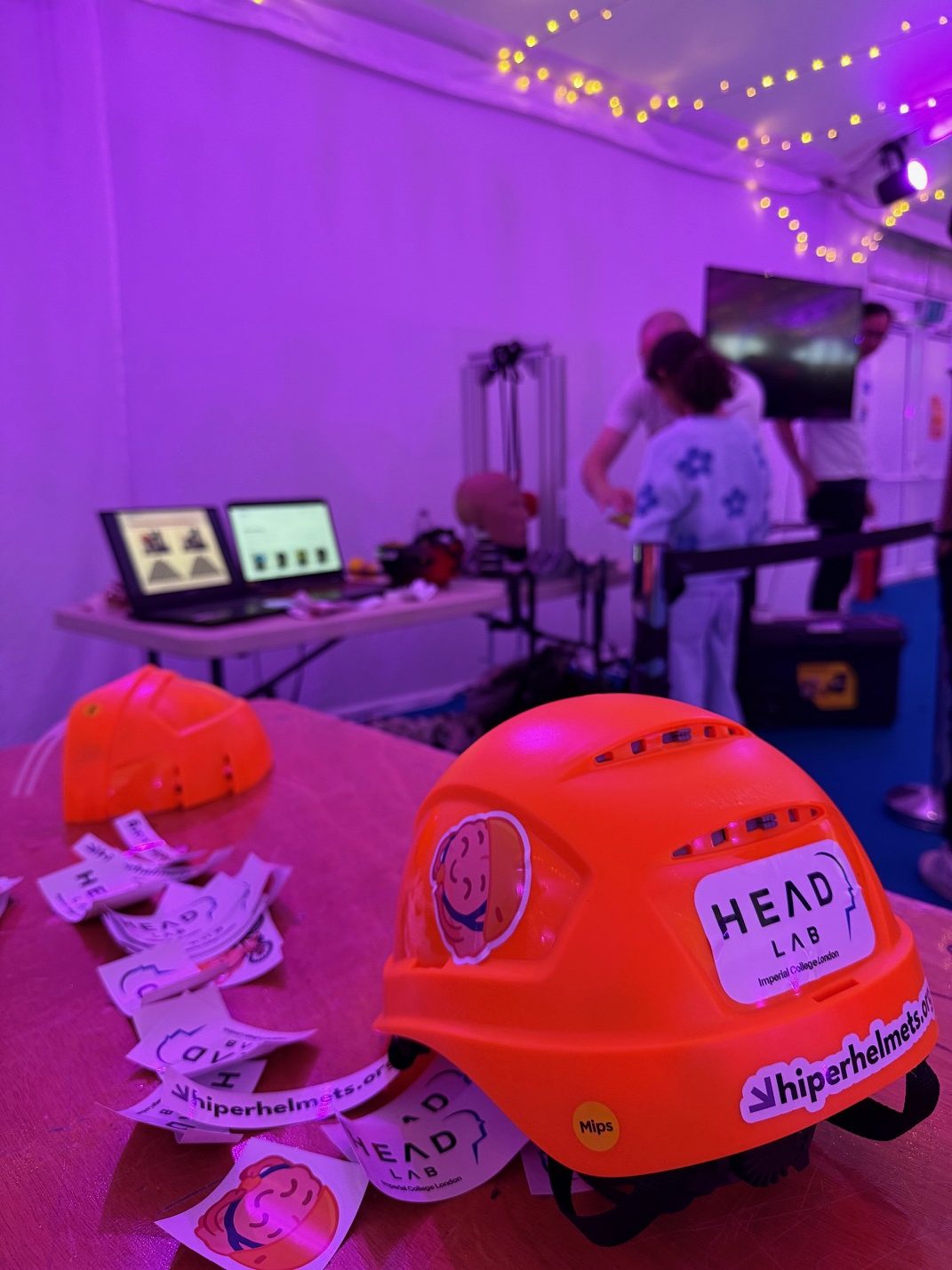 A HIPER-rated helmet and HEAD Lab stickers on the lab's stand at the Great Exhibition Road Festival 2025, with the impact rig behind.