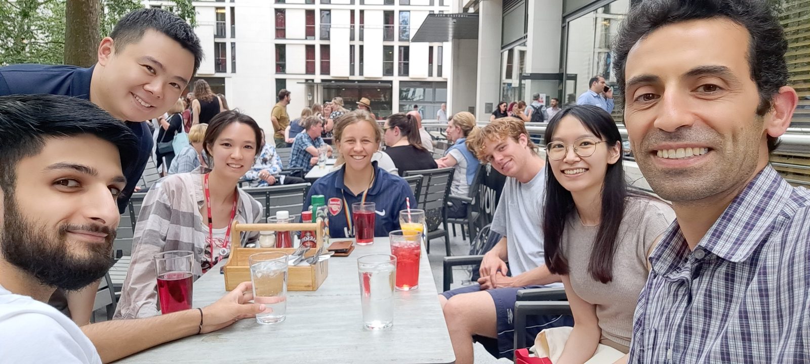 The lab around a long outdoor table with drinks on a summer evening.