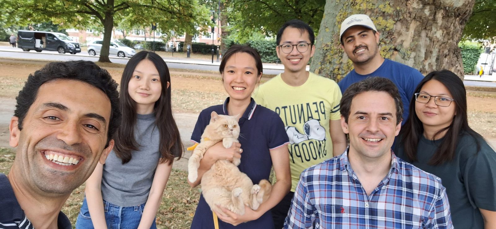 Members of the lab together in a park on a sunny afternoon, one holding a small cat.