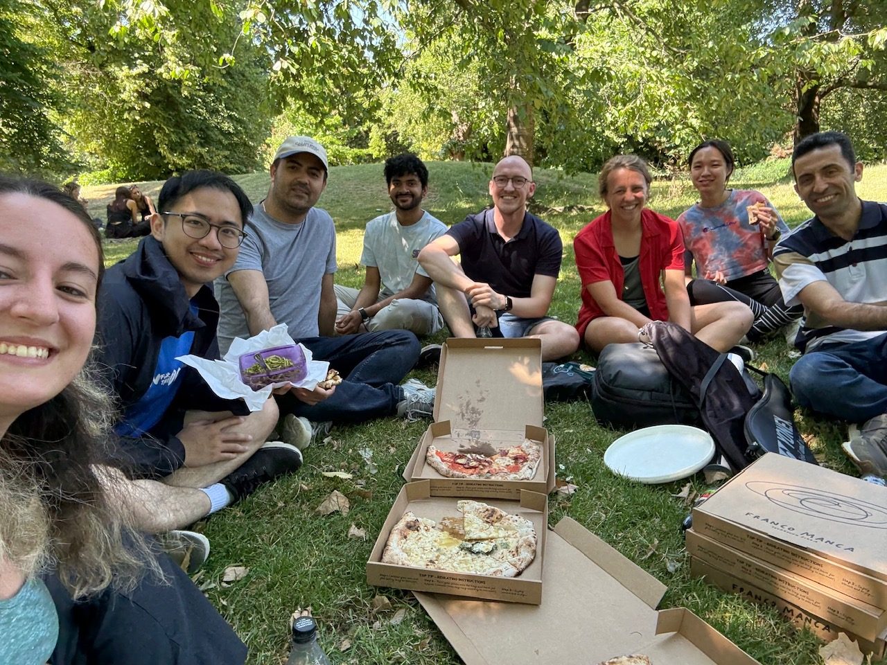 The lab sitting on the grass in a park around open pizza boxes.