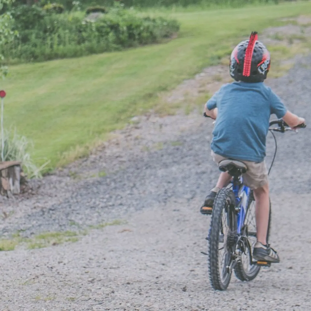 A child cyclist wearing a helmet rides along a gravel path, seen from behind.