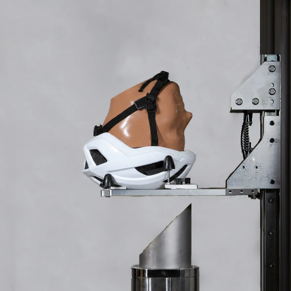 A cycle helmet fitted on a headform, mounted on the lab's oblique-impact test rig above an angled anvil.